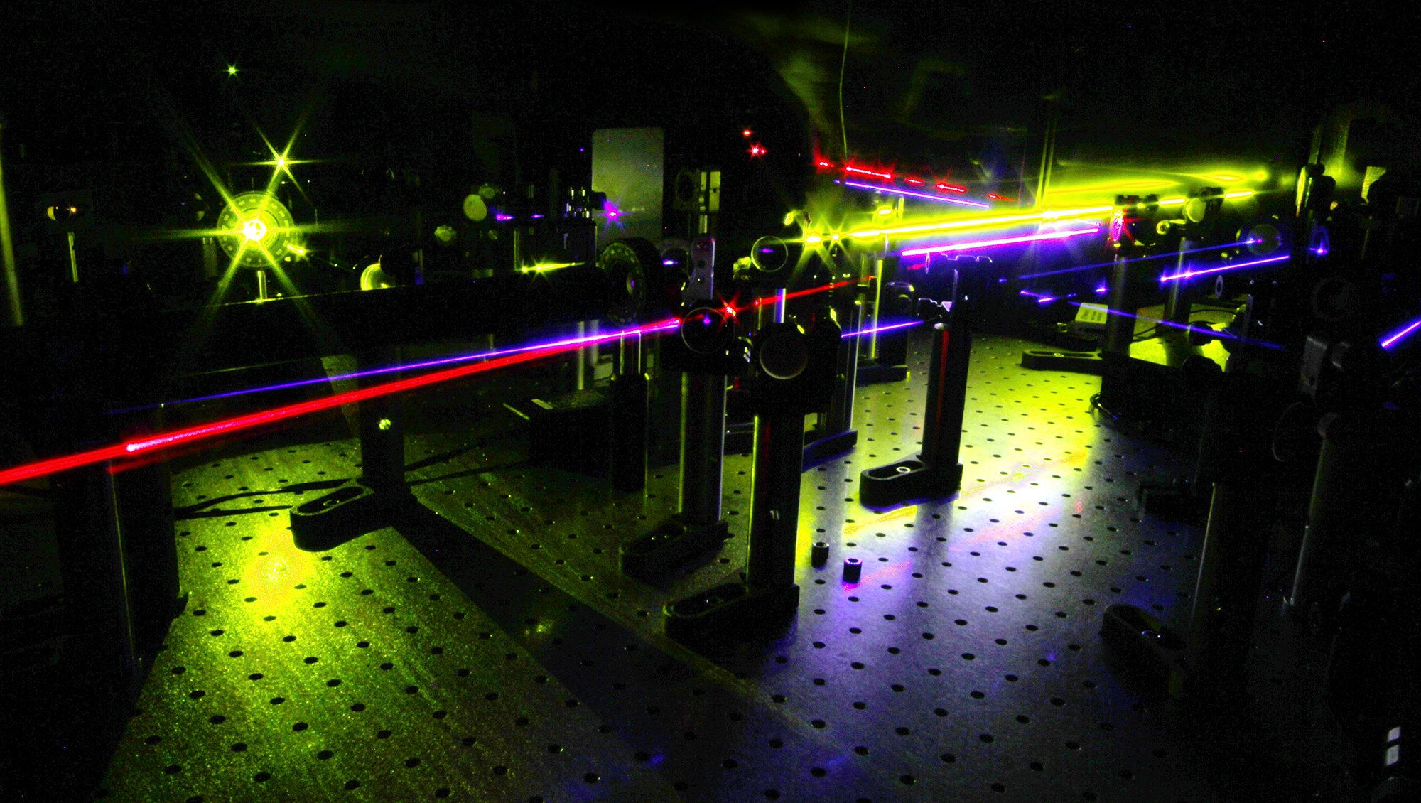 Photograph of a femtosecond optical laser laboratory with mirrors, lenses, and optical components arranged on an optical table for ultrafast spectroscopy experiments.